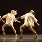 Dancers in white against black stage backdrop