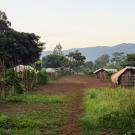 Looking down the middle of an African village with wooden buildings and mountains in the distance.