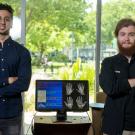 Two men surround a desktop computer with illustration on it