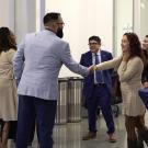 in a mixer setting, academics in professional dress introduce each other by shaking hands. 