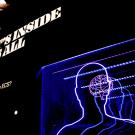 Museum exhibit with layered neon-blue outlines of human heads and illuminated signage