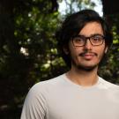 Casual outdoor portrait of a young man with glasses smiling against leafy background