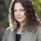 A portrait of Karima Bennoune standing outside with some green bushes in the background.