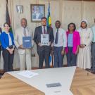 12 people dressed in business attire stand and face camera around a board room table. Two men in the center hold up folders and a document. 