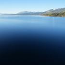 Calm deep-blue Lake Tahoe with forested shore and distant mountains under clear sky