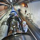 A worker in a helmet inspects large metallic pipes inside a tunnel.