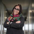 Smiling woman in glasses and colorful scarf, arms crossed in an office corridor