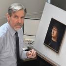 Conservator with gray hair restoring a small framed portrait on an easel