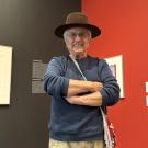 Male artist in hat stands in front of his work in a museum