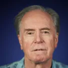 Portrait photograph of person with gray hair, blue patterned shirt, neutral expression
