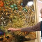 A woman shows a large painting of several animals
