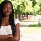 Student stands with her arms crossed with campus in the background