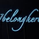 Blue neon lights reading "I belong here" against black text.