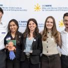 Six smiling people in business casual holding awards and a plush mascot against logo backdrop