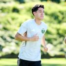 A young athlete jogging on a bright green field, wearing a white jersey and black shorts.