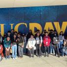 Group of students posing in front of large gold UC Davis sign on blue wall