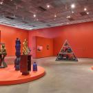 Contemporary gallery with bright orange walls, large colorful sculptural figures on round plinths