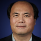 A person wearing a dark blazer and light shirt on a dark blue background.