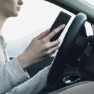 A young woman stops her car to look at her mobile phone.