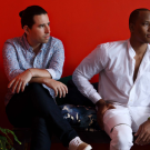 Two men sitting on couch with red background