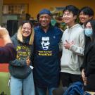 Chancellor May in "Moonlioght Breakfast" apron, flanked by students, having their picture taken