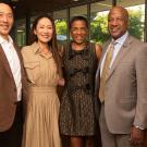 Group photo of four smiling adults in business attire standing indoors by a window