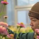 Young person in brown beanie focused while tending pink flowers in greenhouse — photo