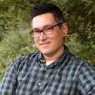 Man in green-and-blue checkered shirt sits on arboretum bench.