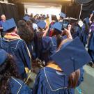 Graduates walk toward doorway in arena as volunteers in purple T-shirts cheer