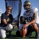 Cori, a black labrador retriever, poses for a photo with a football kicker and faculty member