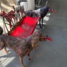 Three painted dog sculptures linked by a red bench on a sunlit concrete floor