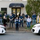 Fleet Services crew, spaced out, posed, behind two UC Davis cars