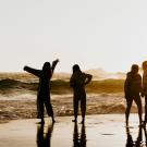 Five silhouetted people on wet sand at sunset, beach photo with waves behind