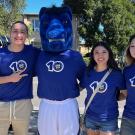 Three people smiling with Gunrock mascot outdoors, wearing blue shirts with 10 logo