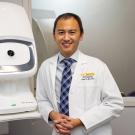 Glenn Yiu, in white lab coat, with ophthalmology equipment, UC Davis Health