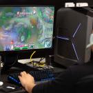 Person wearing headset plays multiplayer PC game at desktop with lit tower and water bottle