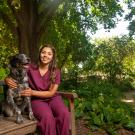 A student in scrubs poses next to a spotted dog in the leafy UC Davis Arboretum.