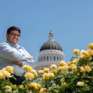 A student poses in front of the state capitol dome and yellow roses. 