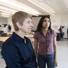 Two women look at a poster with others in the background.