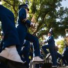 Low-angle of marching band in navy uniforms and white shoes stepping under sunlit trees