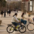 Two women biking with the promenade in the background