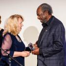 Two women present trophy to a man, on stage