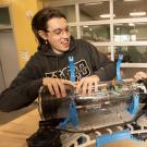 Two students smiling as they work on a blue-accented robot on a table.