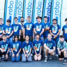 Group of people wearing blue matching T-shirts poses in front of flags that read "RoboSub"
