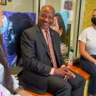 Chancellor Gary S. May talks with two students, seated, inside the Student Community Center