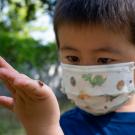 Boy in mask observes ladybag on his hand.