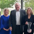 Five people pose, in a line, one holding glass trophy