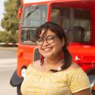 A female student stands in front of a double-decker Unitrans bus