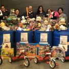 Group of people stand in front of large pile of new toys and tricycles collected during a toy drive.
