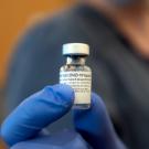 Gloved hand holds empty vial of COVID-19 vaccine.